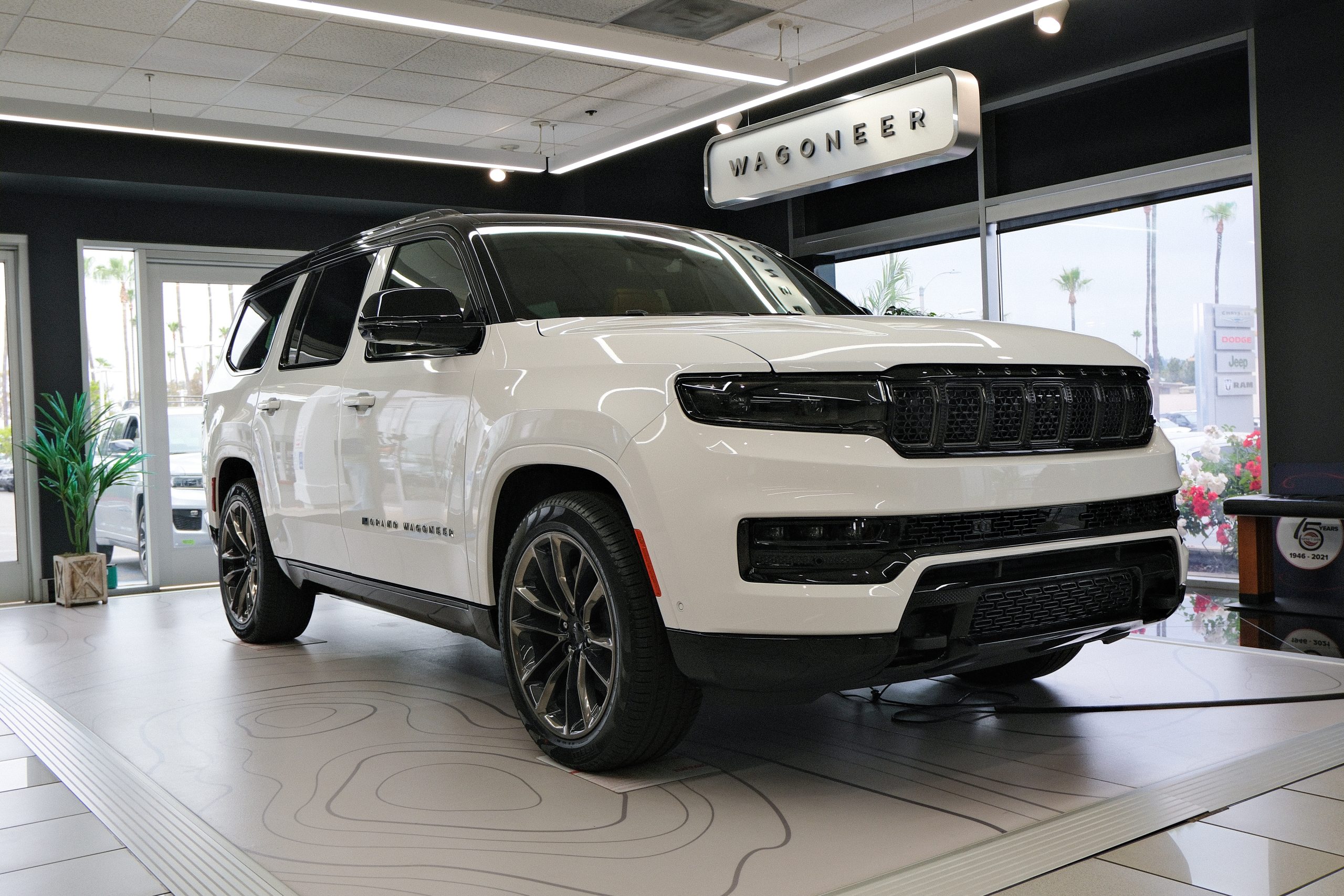 White Jeep Wagoneer SUV displayed inside Tuttle-Click showroom with modern lighting.